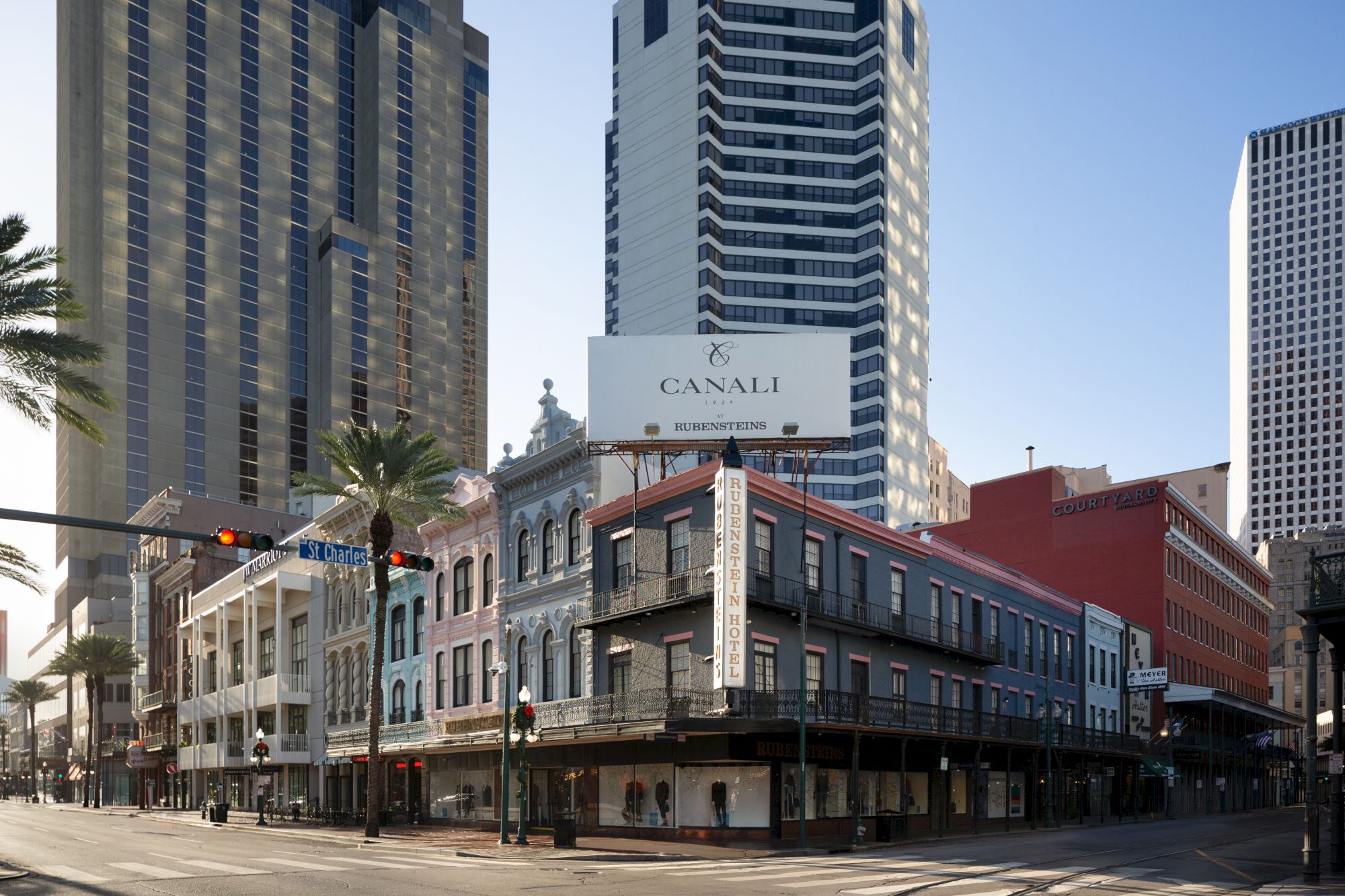 The image shows a city street corner with historic and modern buildings, featuring a billboard for "Canali." There's a traffic light and palm trees.