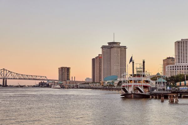 A waterfront scene with a paddleboat, tall buildings, and a bridge at sunset on a calm river.