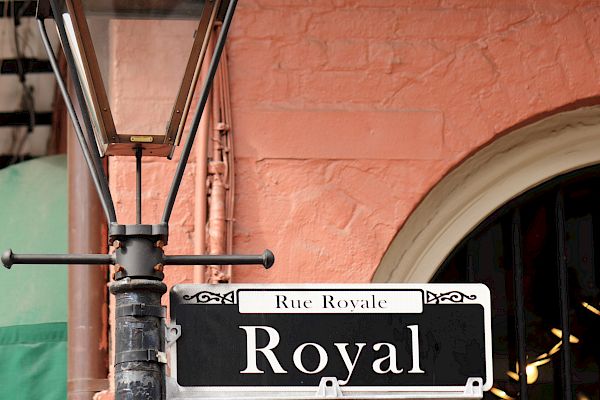 A street sign for "Royal" next to a vintage lamp post against a pink brick wall.