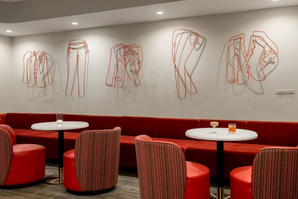 A modern lounge with red seating, white round tables, and artistic metal sculptures resembling clothing on the wall for decoration.