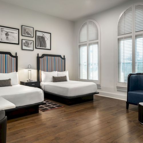 A hotel room with two beds, striped headboards, a small couch, and wall art. There's wooden flooring and arched windows.