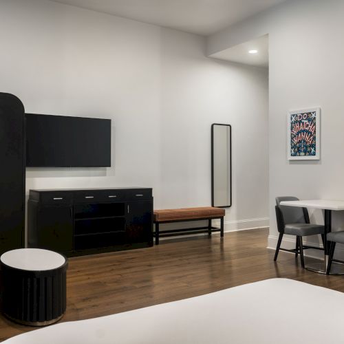 A modern room with a TV, wardrobe, table and chairs, wall art, and a mirror on a wooden floor.