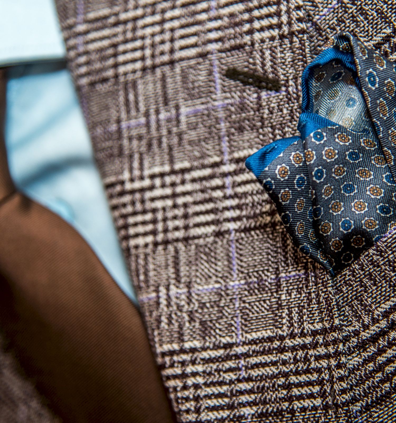 A close-up of a stylish checkered suit with a brown tie and a blue patterned pocket square, providing a classic, formal look.