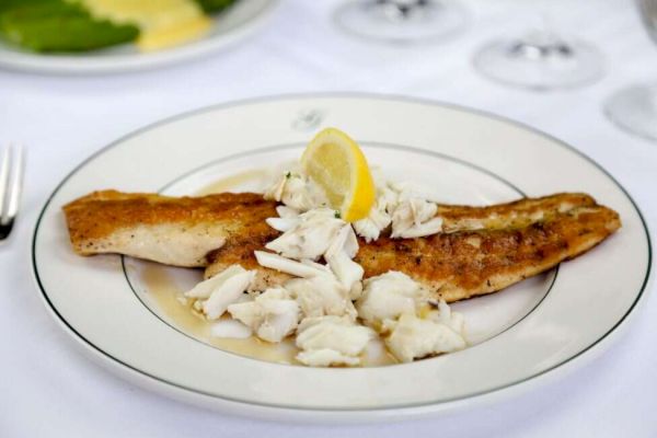 A plate of grilled fish topped with crab meat and a lemon wedge.