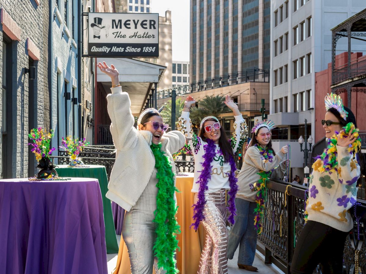 People in festive attire celebrating on a balcony with colorful decorations and city buildings in the background.