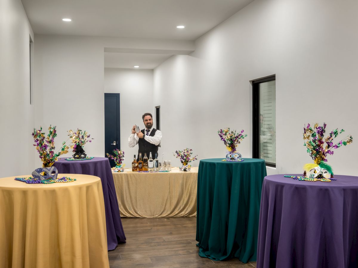 A bartender is preparing drinks in a room with festive, decorated tables covered in yellow, green, and purple tablecloths.