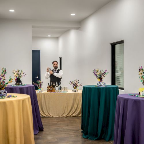 A bartender shakes a cocktail behind tables adorned with Mardi Gras-themed masks and decorations in a brightly lit room.